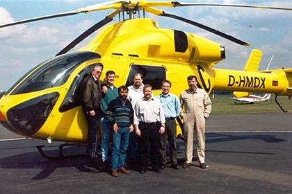 Sieben Männer stehen vor einem gelben Helikopter